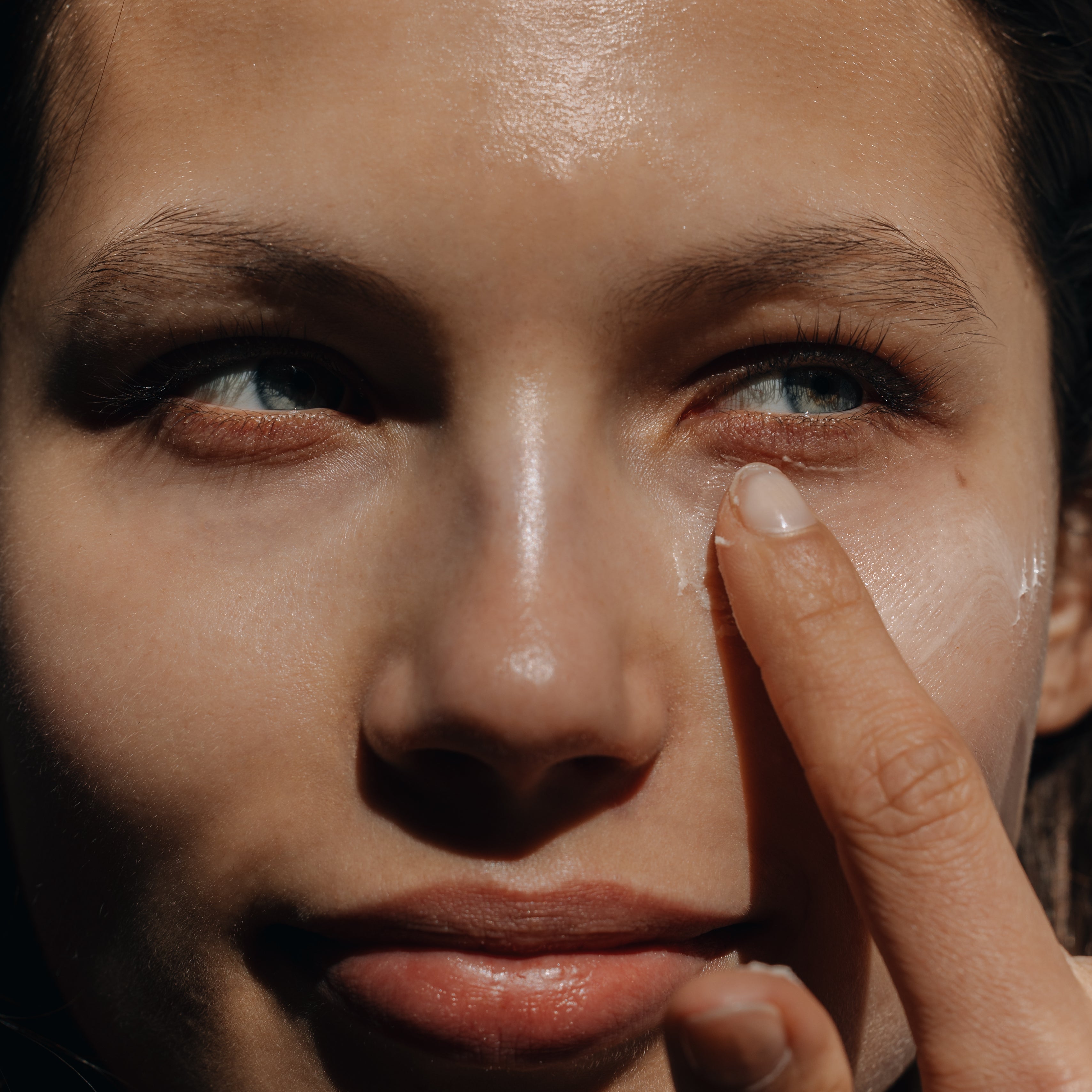 Woman applying cream under her eye in a sunny setting
