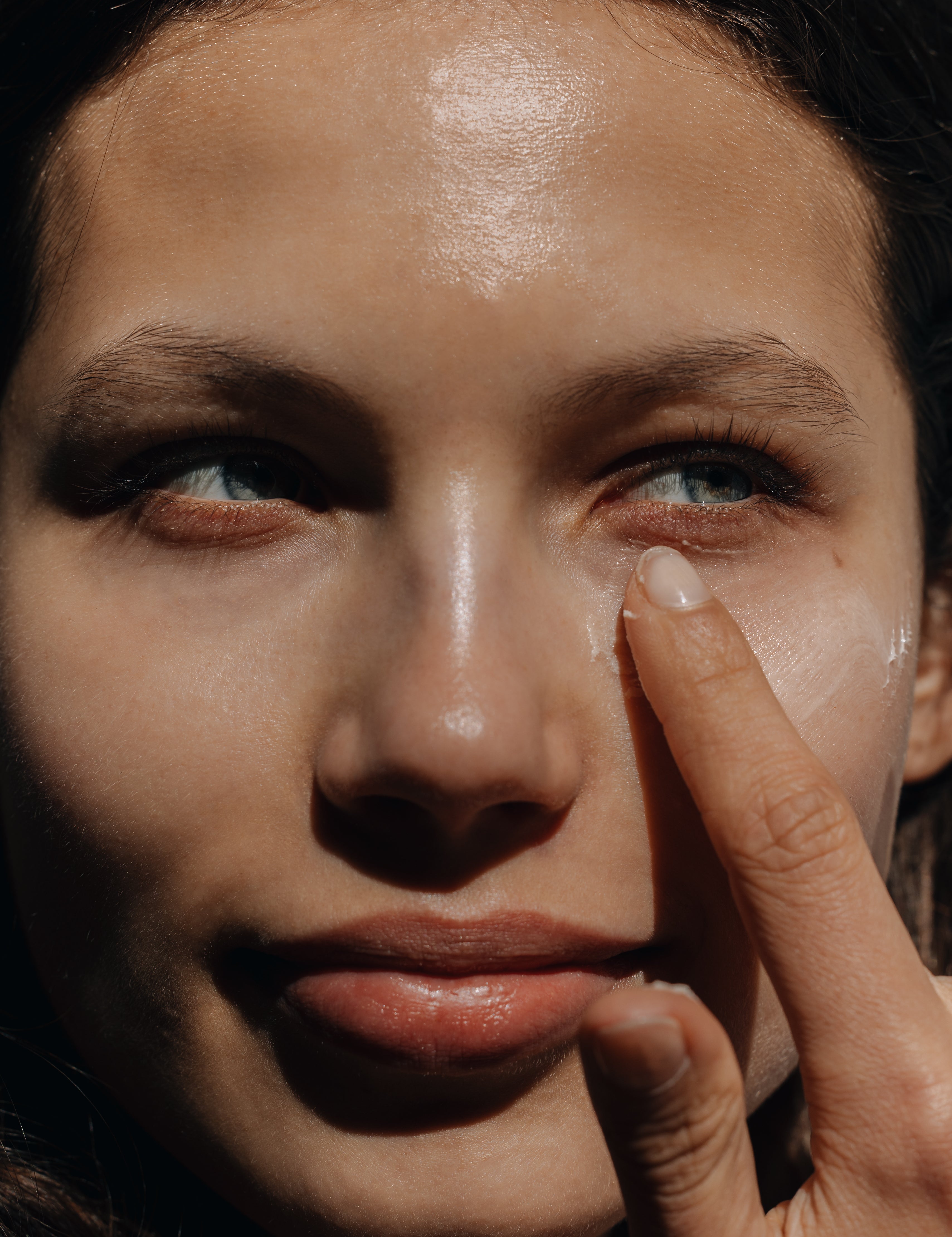 Woman applying cream under her eye in a sunny setting